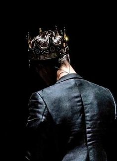 a man in a suit with a crown on his head looking down at the ground