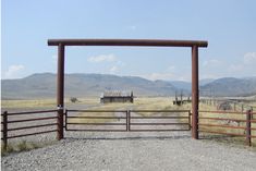 an open gate on the side of a dirt road with mountains in the back ground