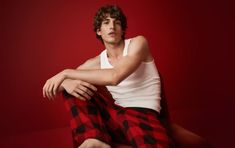 a man sitting on top of a red chair wearing plaid pants and a tank top