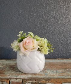 a white vase filled with flowers sitting on top of a wooden table next to a gray wall