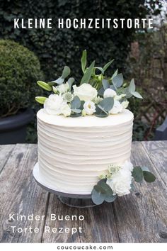 a small wedding cake with white flowers and greenery on top is sitting on a wooden table