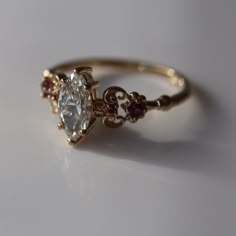 a gold ring with an oval cut diamond and garnets on the side, sitting on a white surface