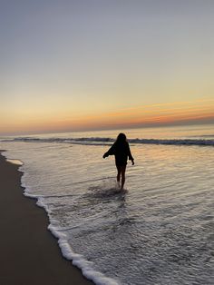 a woman walking into the ocean at sunset