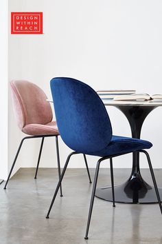 two chairs sitting at a table with a round top and black metal legs, in front of a white wall