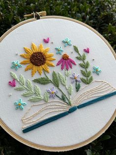 an embroidered book with flowers and butterflies on it is sitting in the grass next to some bushes