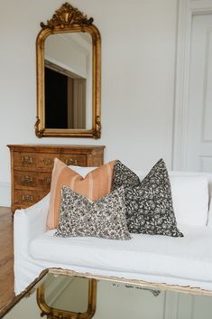 a white couch with pillows on it in front of a mirror and wooden dressers