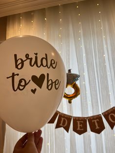 a person holding a white balloon with the words bride to be written on it in front of a curtain