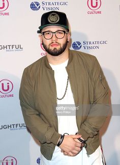 a man wearing glasses and a hat standing in front of a wall