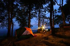 a tent is set up in the woods at night with its lights on and some people standing around it