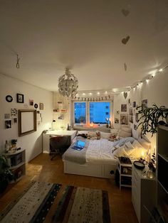 a bedroom with a bed, desk and television in it's center area is lit up by lights strung from the ceiling