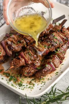 someone is pouring sauce on top of some meat skewers with onions and herbs