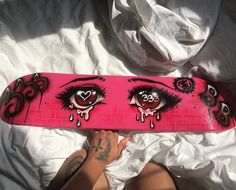 a person laying on top of a bed holding a pink snowboard with eyes painted on it