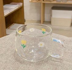 a glass cup with yellow flowers on it sitting on top of a cloth covered table