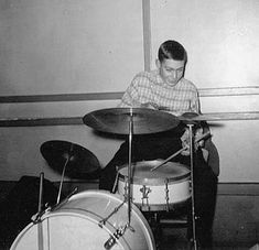 a man sitting in front of a drum set on top of a floor next to a wall