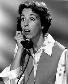 a woman holding a telephone to her ear and making a surprised face as she talks on the phone