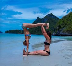 two women in bikinis doing yoga on the beach