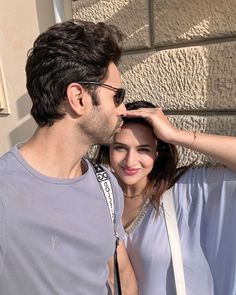 a man and woman standing next to each other near a wall with their hands on their foreheads