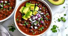 two bowls filled with chili and avocado on top of a white countertop