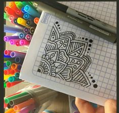 a person holding up a paper with an intricate design on it next to crayons and markers