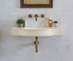 a bathroom sink sitting under a mirror next to a potted plant and soap dispenser