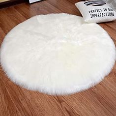 a white round rug sitting on top of a hard wood floor next to a pillow