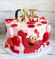 a birthday cake with the number one on it and an elmo character holding balloons