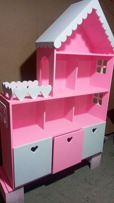 a pink and white doll house shelf with drawers on it's sides, in front of a brown wall