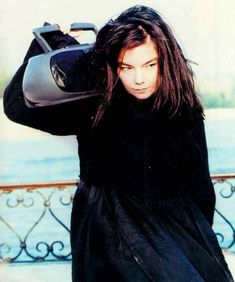 a woman with long hair carrying a suitcase over her shoulder and looking at the camera