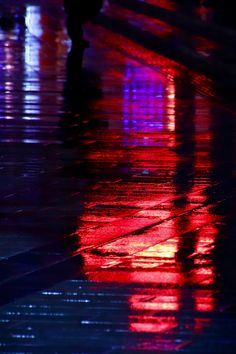 people walking down the street at night with their umbrellas on and lights reflecting in the wet pavement