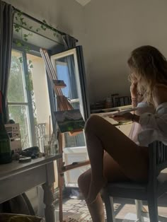 a woman sitting at a desk in front of a window with an easel next to her