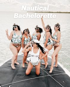 a group of women in bathing suits standing on the back of a boat with their arms up