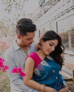 a man and woman standing next to each other in front of a building with pink flowers