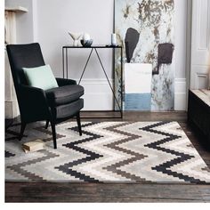 a black chair sitting on top of a wooden floor next to a white and gray rug