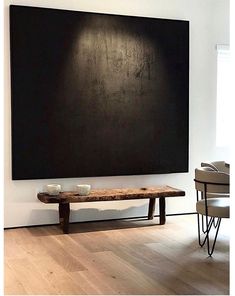 a wooden bench sitting in front of a large black piece of art on the wall