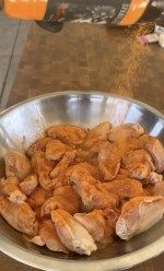 a metal bowl filled with chicken sitting on top of a table next to an orange bottle