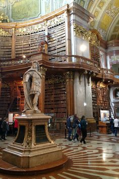 people are standing in the middle of a library with many bookshelves and statues