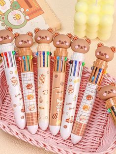 four pens with teddy bears on them sitting in a basket next to a book and some candy