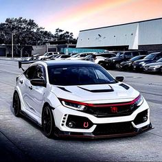 a white honda civic type car parked in front of a parking lot with other cars