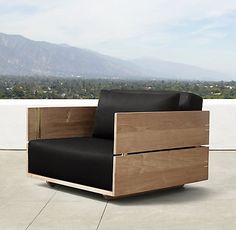 a wooden chair sitting on top of a cement floor next to a wall with mountains in the background