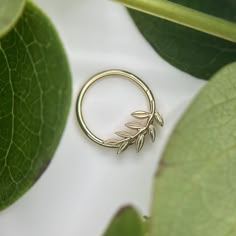 a gold ring with leaves on it sitting next to some green leafy plants and greenery