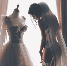 a woman standing next to a dress on a mannequin in front of a window