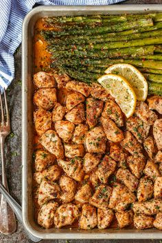 chicken and asparagus on a sheet pan with lemon wedges next to it