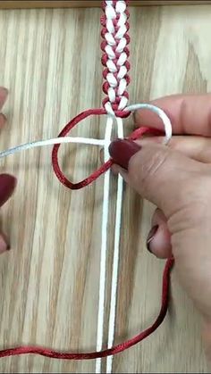 two hands are working on an object with red and white yarn, while another hand is holding the string