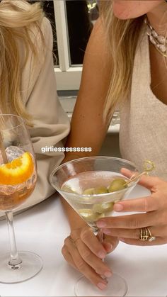 two women sitting at a table with drinks in their hands and one holding an orange slice