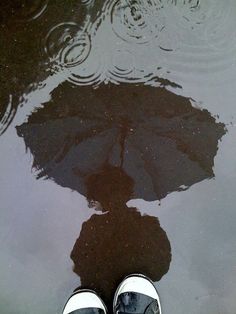 a person standing in front of a puddle with an umbrella on the ground next to it