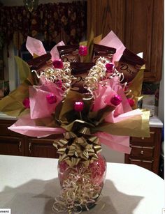 a vase filled with lots of candy wrapped in pink and gold paper wrappers on top of a table