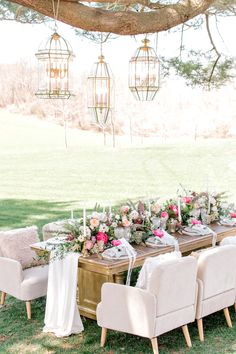 a long table with white chairs and pink flowers is set up under a large tree