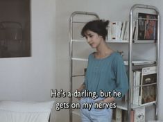 a woman standing in front of a book shelf next to a bed with books on it