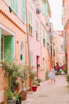 a woman in a white dress walking down an alley way with potted plants on either side