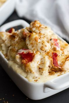 a white dish filled with macaroni and cheese covered in sauce on top of a table